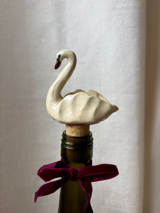 Swan-shaped bottle stopper on a bottle with a purple ribbon against a plain background