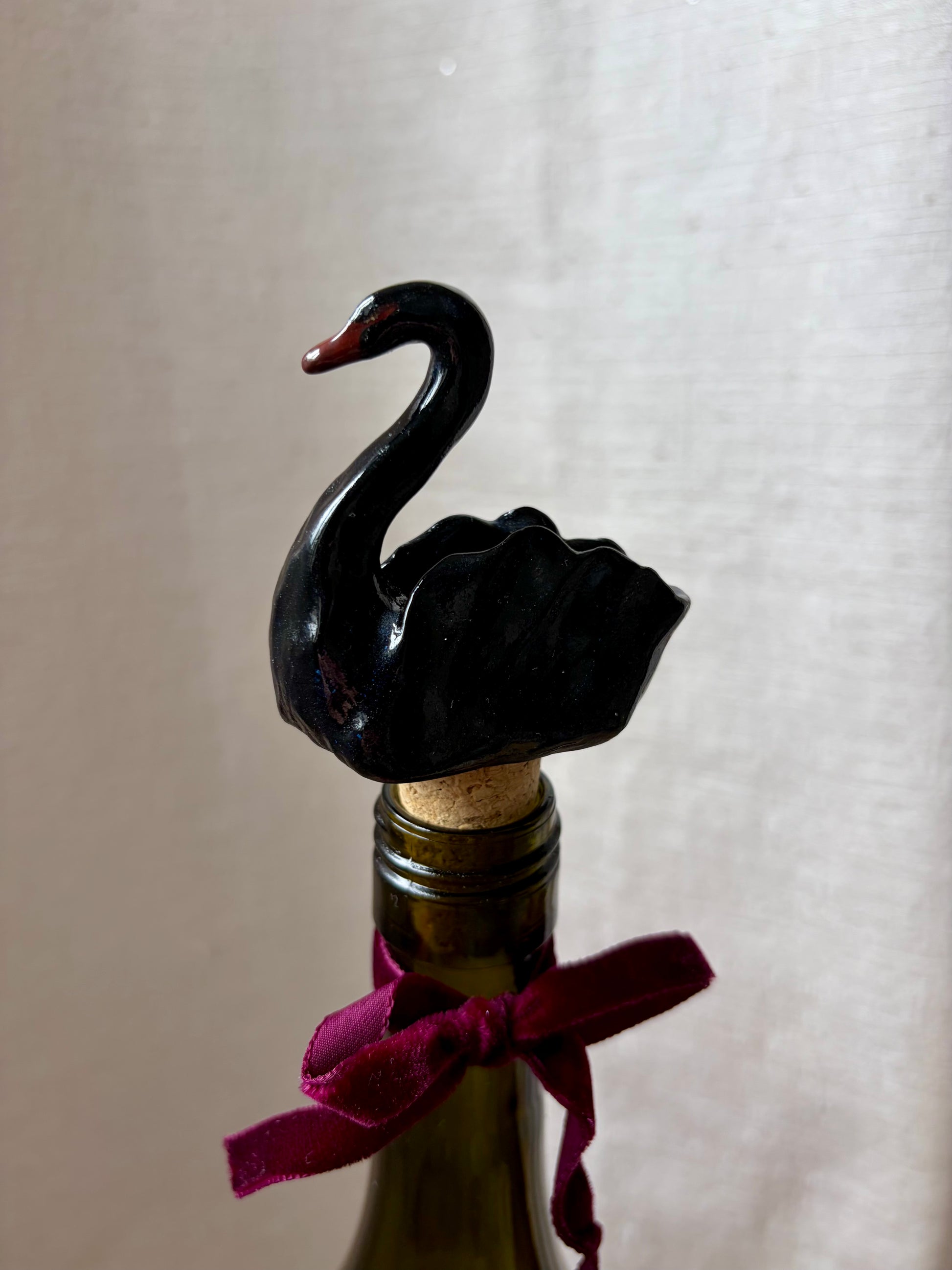 Black swan bottle stopper on a wine bottle with a purple ribbon against a white background