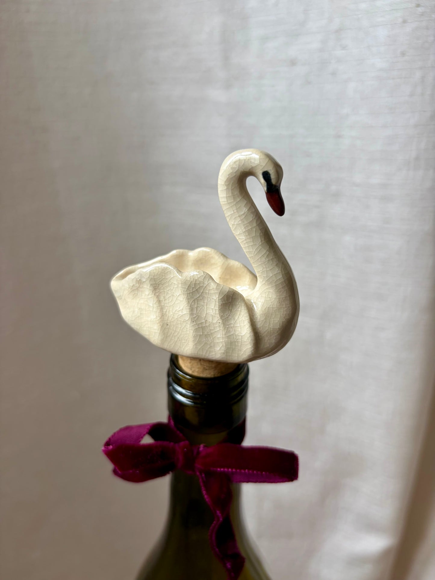 Decorative swan bottle stopper on a bottle with a purple ribbon against a plain background